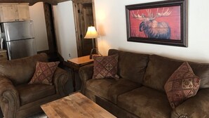 Un salon chaleureux avec un canapé en cuir marron, une table basse en bois et un tableau représentant un élan, encadré, accroché au mur.