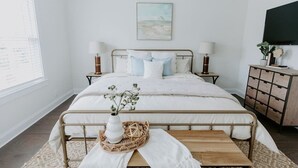 Un dormitorio ordenado con cama, mesitas de noche, televisión y ventana.