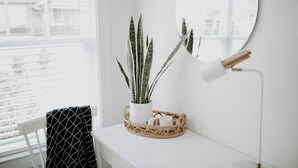 Habitación blanca con una planta en maceta, un espejo redondo y una lámpara de pie sobre una superficie blanca.