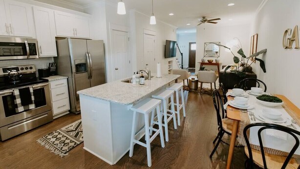 Una cocina moderna con gabinetes blancos, electrodomésticos de acero inoxidable y una isla central con taburetes de bar.