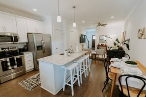 A modern kitchen with white cabinets, stainless steel appliances, and a central island with bar stools. - NEW Maple Manor | Murfreesboro Luxury Townhouse (Murfreesboro)