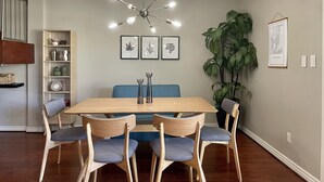 A dining area with a wooden table, four chairs, a blue sofa, a ceiling light fixture, and a large green plant. - Come fall in LOVE with Chateau MB (Scottsdale)