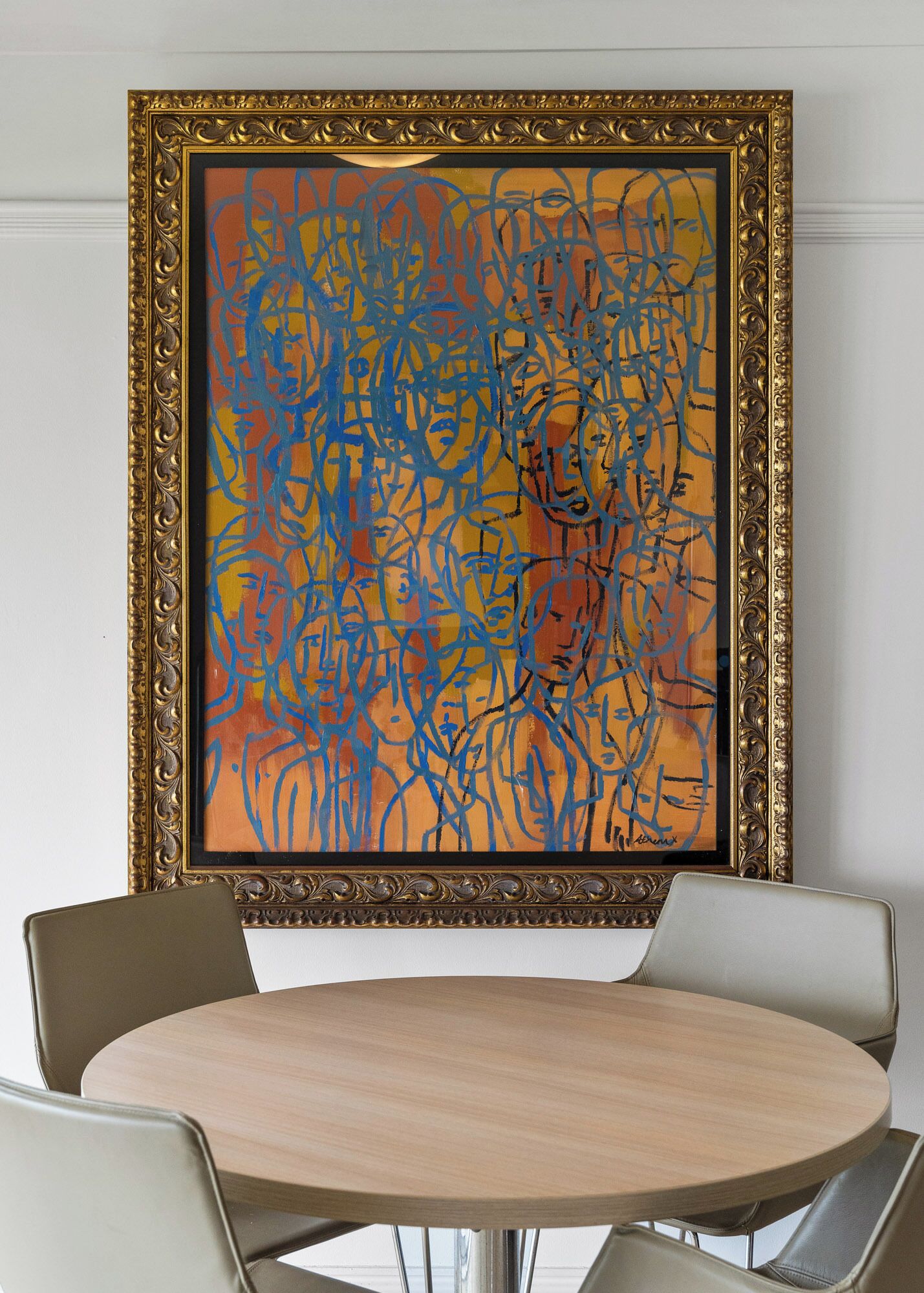 A framed abstract painting on a wall above a round table with four chairs.