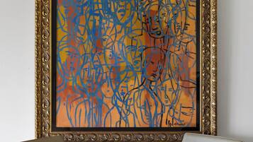A framed abstract painting on a wall above a round table with four chairs.
