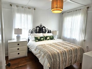 Ein Schlafzimmer mit einem Bett, zwei Nachttischen, einer Pendelleuchte und transparenten Vorhängen.