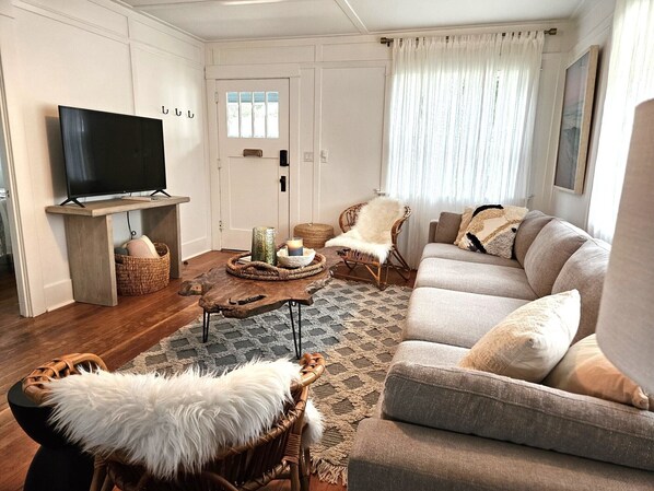 Ein Wohnzimmer mit Fernseher auf einem Holzboden, einer Couch, einem Sessel und einem Teppich.