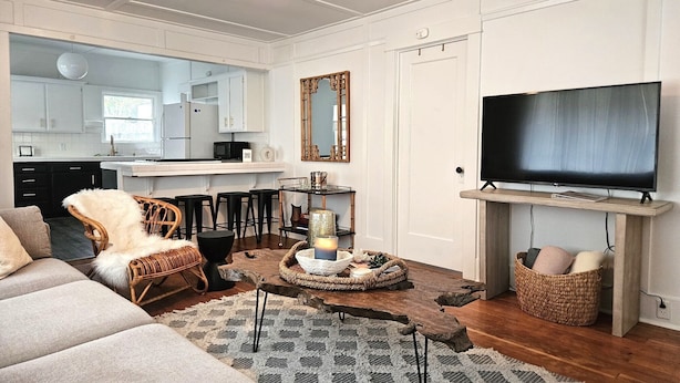 A modern living room with a sofa, a TV, a dining area with stools, and a kitchen in the background. - Charming Beach Cottage, 2 blocks from the water! (Morro Bay)