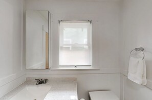 Ein Badezimmer mit großem Spiegel, Fenster, Waschbecken und Handtuchhalter.