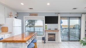 A modern kitchen with a wooden bar, a stone fireplace, and a large window overlooking a deck. - Gorgeous Waterfront Battery Creek Retreat (Beaufort)