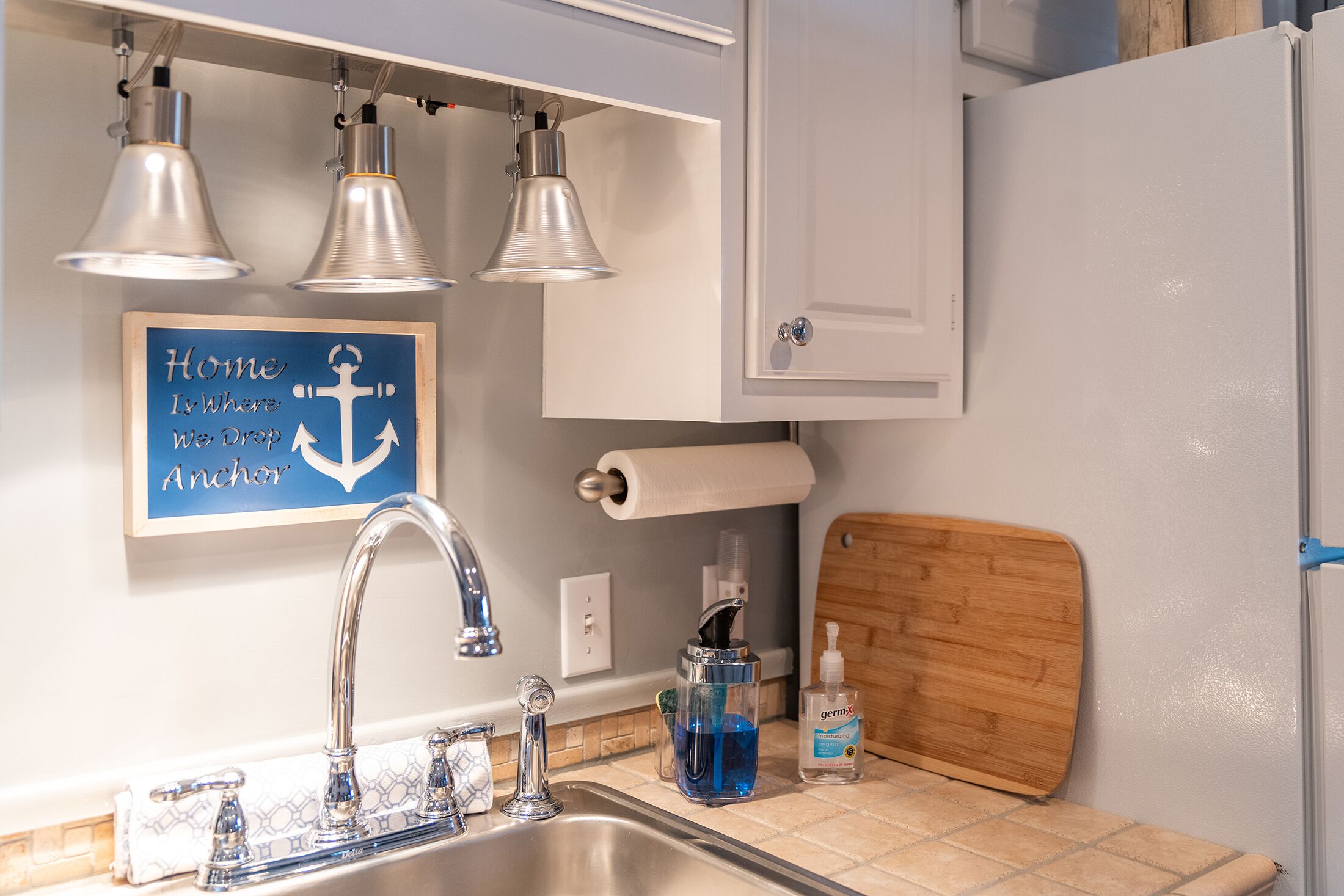 Une cuisine équipée d’un évier, de trois lampes suspendues, d’un rouleau de papier toilette, d’un distributeur de savon et d’une planche à découper en bois.