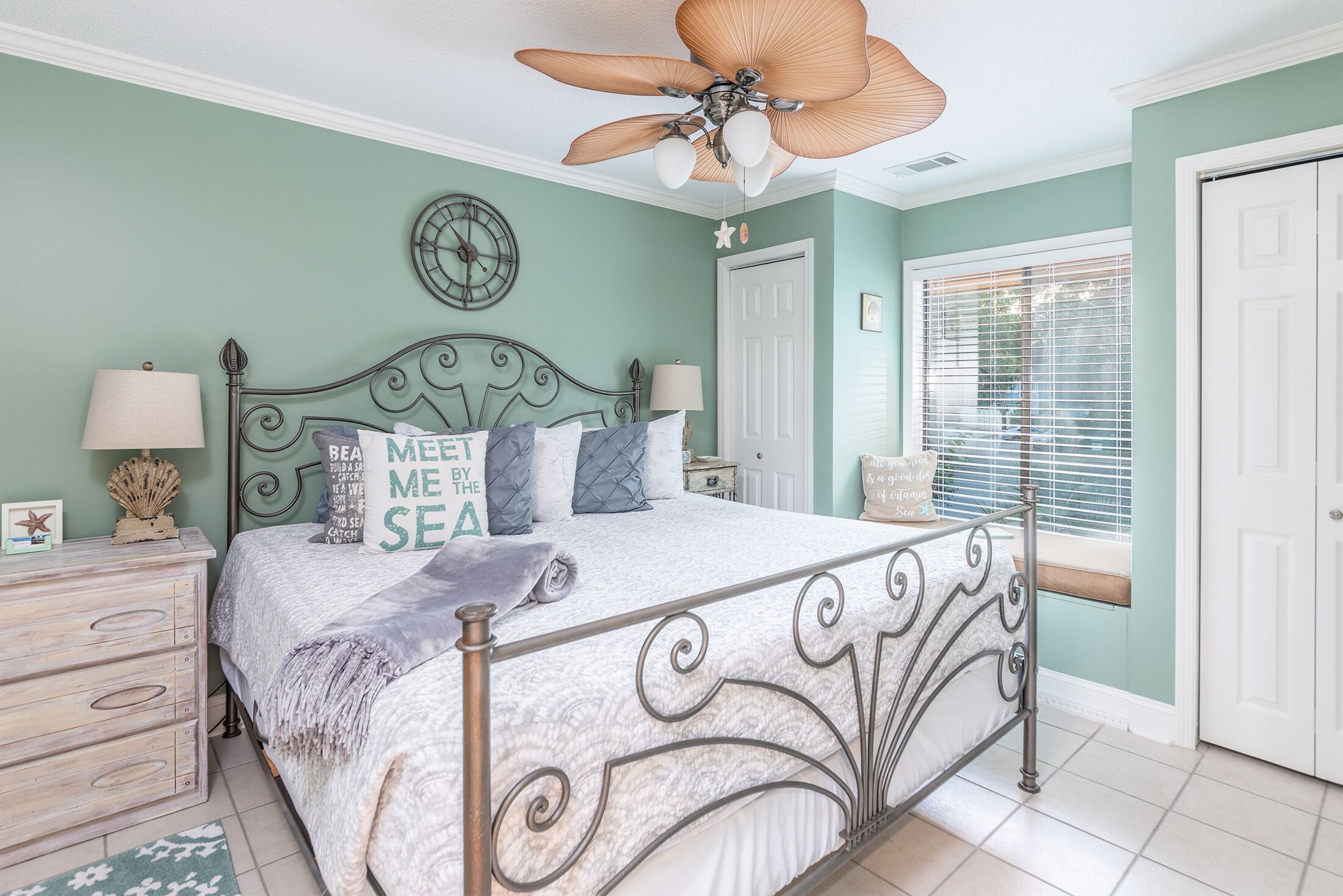 A bedroom with a bed, a ceiling fan, a clock, and a window with blinds.