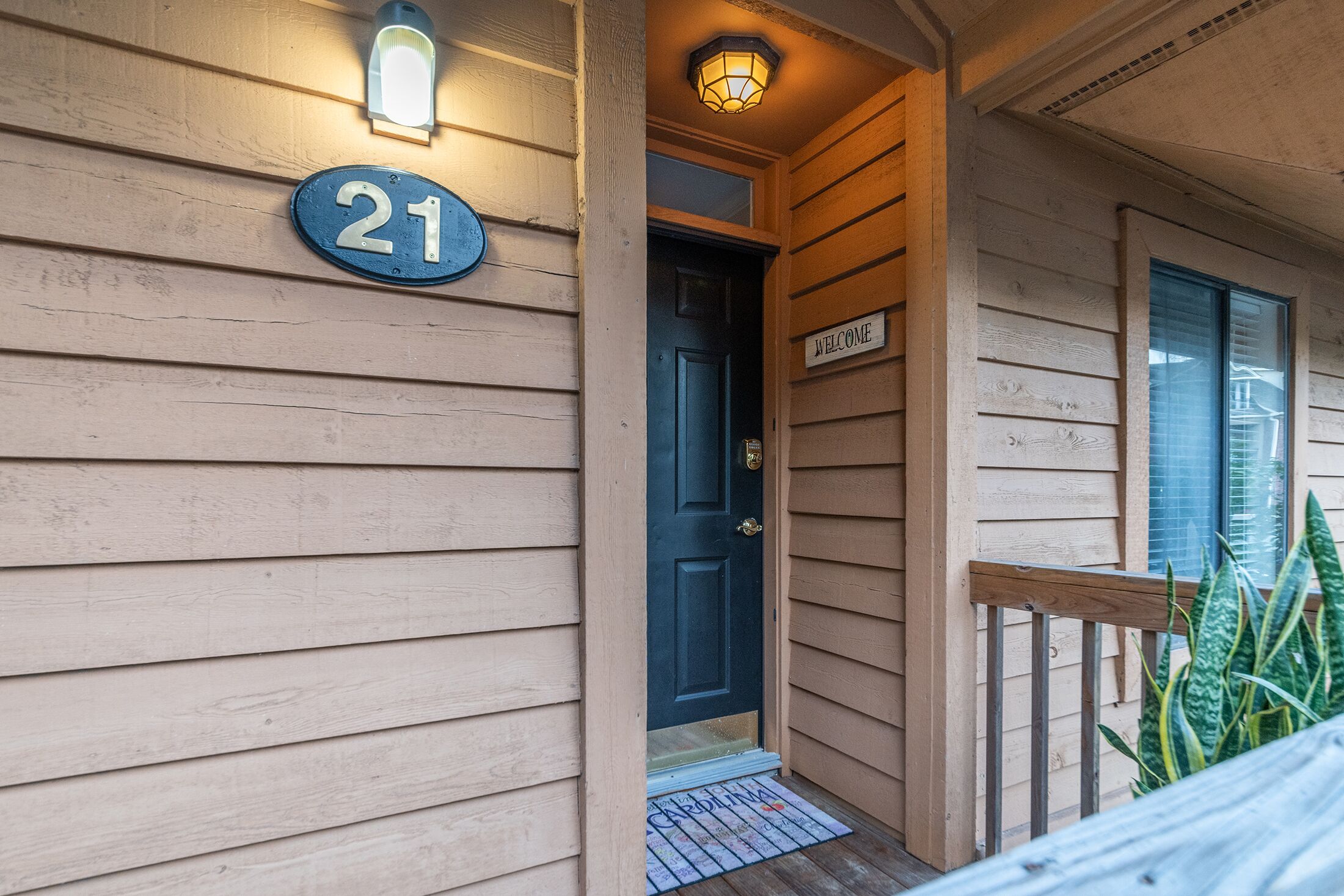 A wooden house with a number '21' sign, a welcome sign, and a door.