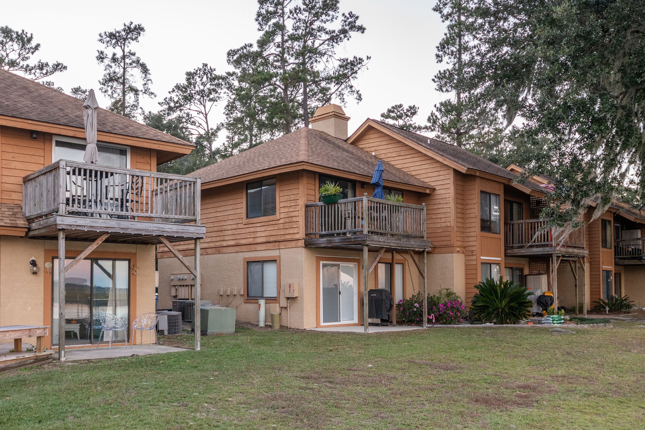 Una hilera de edificios de apartamentos de madera con balcones, mobiliario exterior y un patio cubierto de césped.