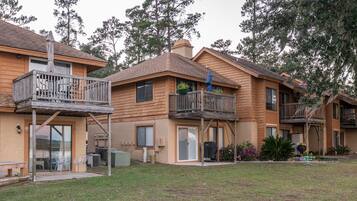 Una hilera de edificios de apartamentos de madera con balcones, mobiliario exterior y un patio cubierto de césped.