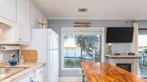 A kitchen with a wooden table, a refrigerator, a sink, cabinets, a window with a view, and a sign that says "Kindness Matters". - Gorgeous Waterfront Battery Creek Retreat (Beaufort)