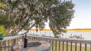 A wooden deck with a round table and chairs, overlooking a body of water with boats. - Gorgeous Waterfront Battery Creek Retreat (Beaufort)