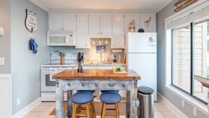 A kitchen with white cabinets, a wooden island with stools, a microwave, and a refrigerator. - Gorgeous Waterfront Battery Creek Retreat (Beaufort)