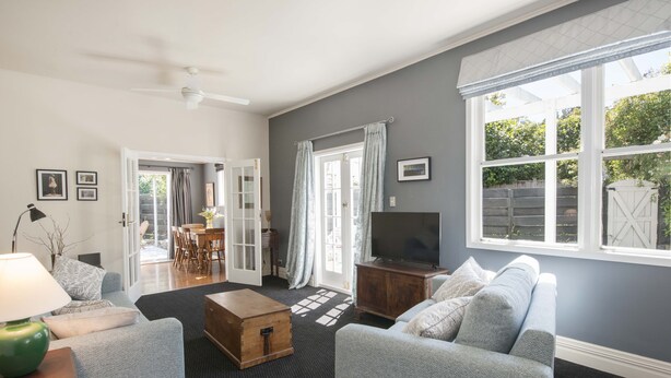 Ein Wohnzimmer mit grauem Sofa, einem Holztisch, einem Fernseher und einem großen Fenster mit Vorhängen.