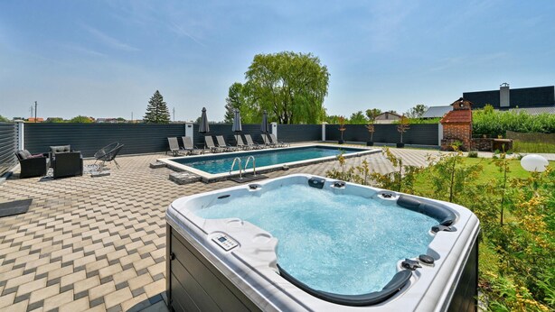 Een achtertuin met een zwembad, lounge stoelen en een jacuzzi.