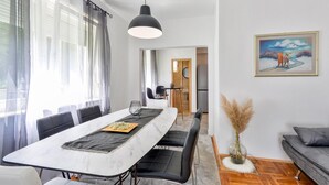 Een moderne woonkamer met een eethoek, een grijze bank, een schilderij en een vaas met gedroogde planten.