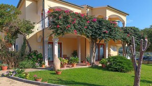 A two-story building with a yellow facade, a covered porch with potted plants, and a well-maintained lawn. - 2 bedroom lovely apartment in Badesi (Badesi)