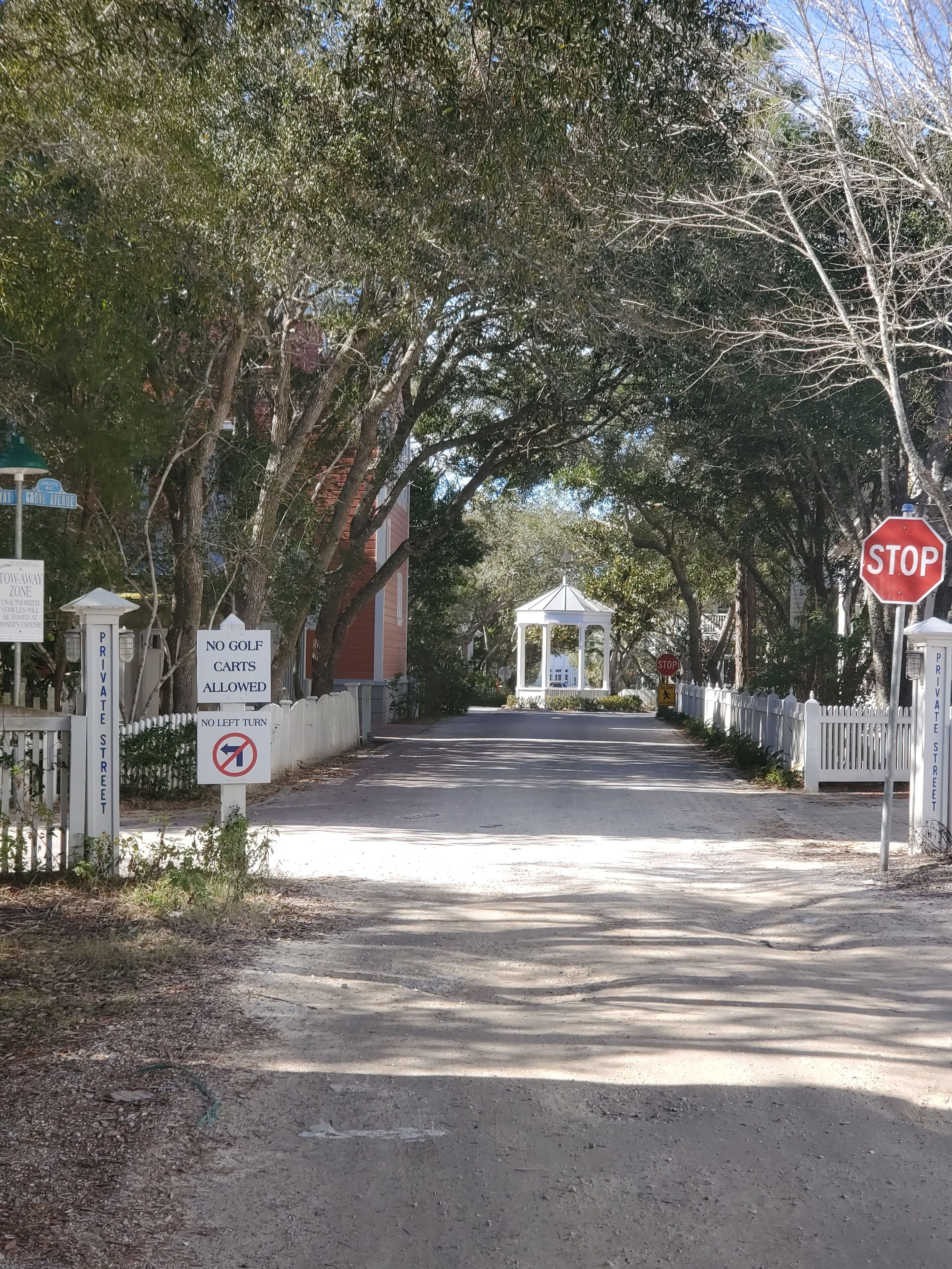 A private street with a stop sign, no left turn sign, and a gazebo in the distance.