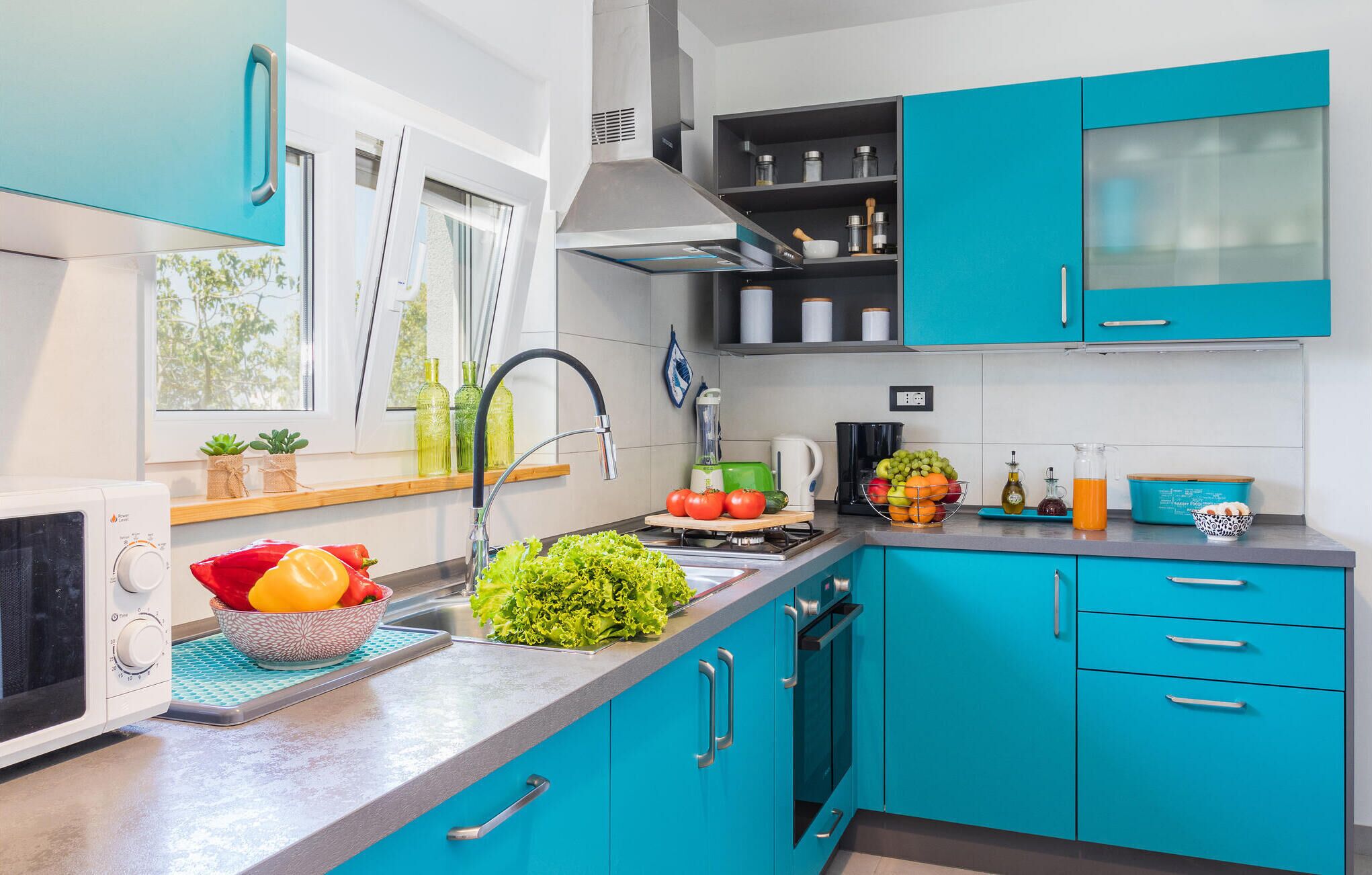 Una cocina moderna con gabinetes color turquesa, un microondas, un lavamanos y distintos utensilios de cocina sobre la encimera.