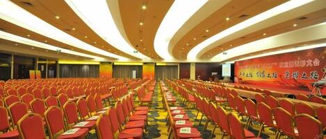A conference room with rows of red chairs and a stage with a banner.