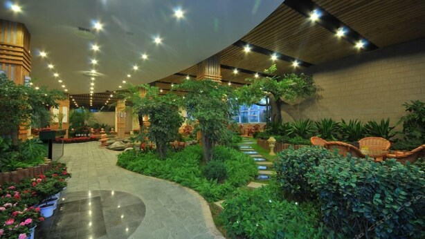 A spacious indoor garden with a curved pathway, potted plants, and wicker furniture. - Long Xin International Hotel (Lanzhou)
