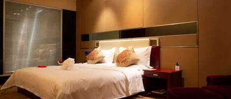 A hotel room with a large bed, a nightstand, a red chair, and a window with blinds.