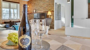 A bottle of wine and a glass on a table in a modern living room with a brick wall and wooden furniture.
