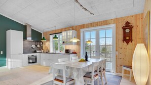 A modern kitchen with white cabinets, a dining area with a white table and chairs, and a wooden interior.