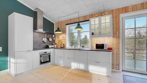 A modern kitchen with white cabinets, a built-in oven, and a large window offering a view of trees.