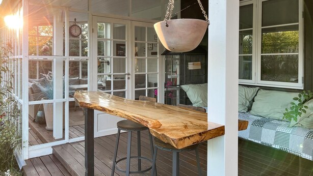A wooden bar stool with a metal frame, a hanging pot, and a window with a view of greenery.
