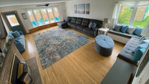 Un salon spacieux avec un grand canapé d ’angle, un pouf rond et un tapis à motifs.