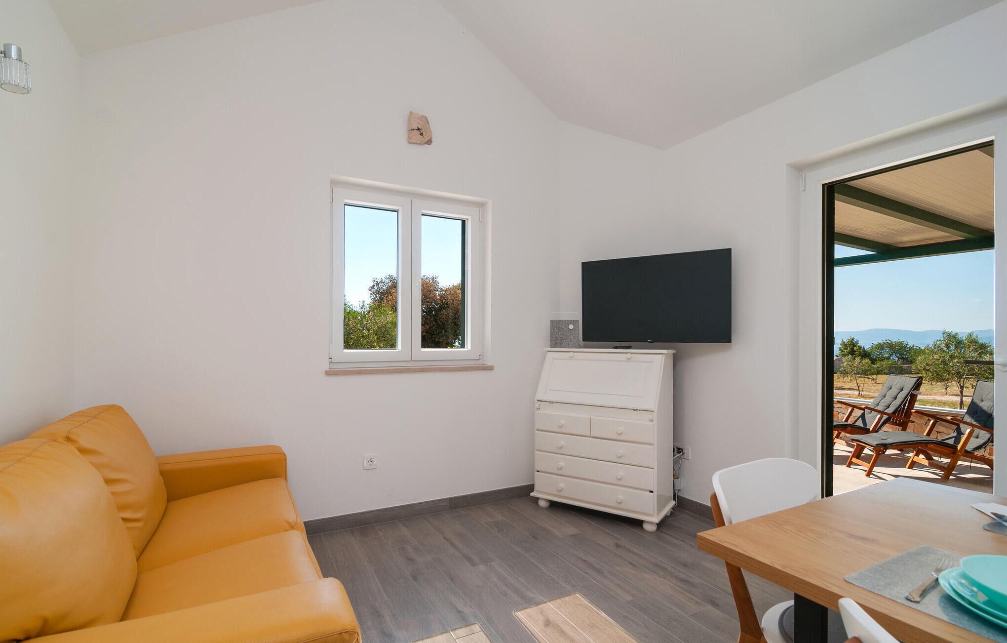 A room with a sofa, a TV on a cabinet, a dining table, and a view of the outdoors.