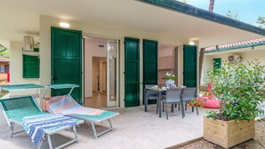 A sunlit outdoor area with two lounge chairs, a table with chairs, and a wooden planter with green foliage. - Stunning home in Lido di Spina FE with swimming pool (Lido di Spina FE)