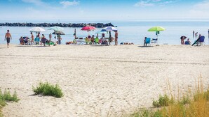 A beach with people relaxing under colorful umbrellas, some sitting on chairs, and a rocky shoreline in the background. - Stunning home in Lido di Spina FE with swimming pool (Lido di Spina FE)