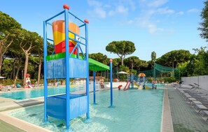 Ein Poolbereich mit Wasserrutsche, Liegestühlen und einer schattigen Sitzgelegenheit.