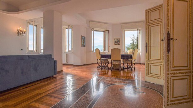 Un salon spacieux avec un canapé bleu, un coin repas comprenant une table et des chaises, de grandes fenêtres et une porte décorative.