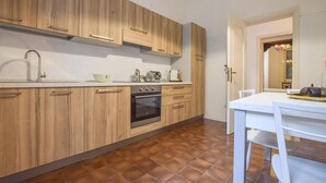 Une cuisine moderne avec des meubles en bois, un four encastré et un coin repas comprenant une table et des chaises blanches.