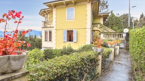 Un bâtiment jaune à deux étages, doté d’un balcon, avec un chemin de pierre menant à l’entrée et offrant une vue sur la verdure environnante.