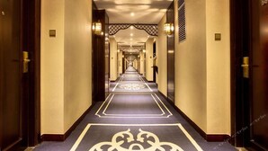 A long, narrow hotel corridor with a patterned carpet, wooden doors, and wall-mounted lights. - Qiaodu Hotel (Jiangmen)
