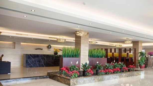 A modern hotel lobby with a marble reception desk, decorative plants, and contemporary lighting fixtures. - Qiaodu Hotel (Jiangmen)