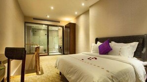 A hotel room with a large bed, a desk, and a glass-enclosed bathroom. - Qiaodu Hotel (Jiangmen)