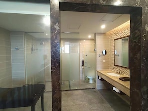 A modern bathroom with a glass shower enclosure, a marble-tiled wall, a wooden vanity, and a large mirror. - Qiaodu Hotel (Jiangmen)