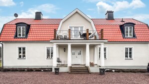 A two-story house with a red-tiled roof, white exterior walls, and a central entrance with a porch.