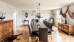 A dining room with a long table, chairs, a chandelier, and antler decorations.