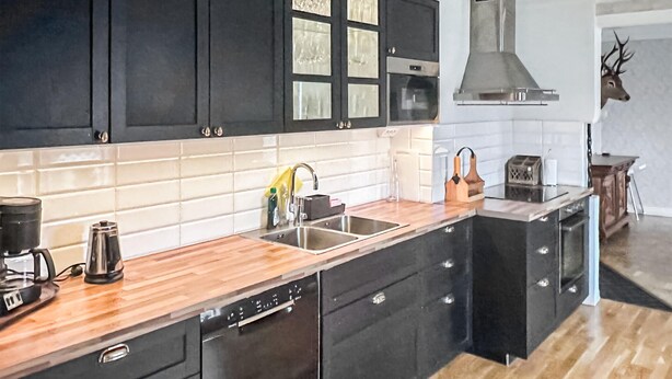 A modern kitchen with black cabinets, a wooden countertop, a dishwasher, and a large stove.