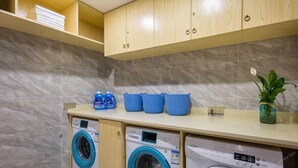 A laundry room with two front-loading washing machines, a countertop with blue baskets, and a potted plant. - Lifeng Tangguo Hotel (Jinhua)